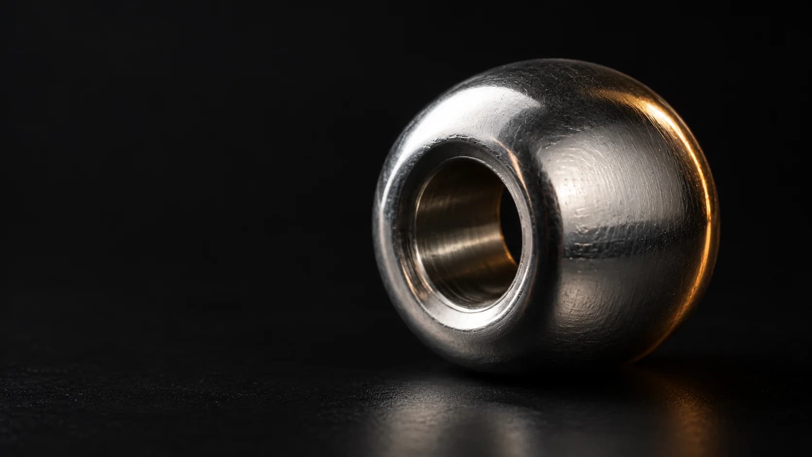 Polished steel abacus bead viewed at an oblique angle.